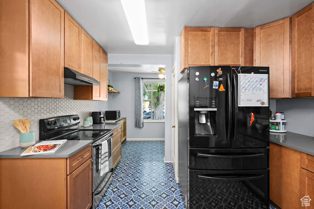 Kitchen featuring black refrigerator with ice dispenser, range with electric cooktop, decorative backsplash, and under cabinet range hood