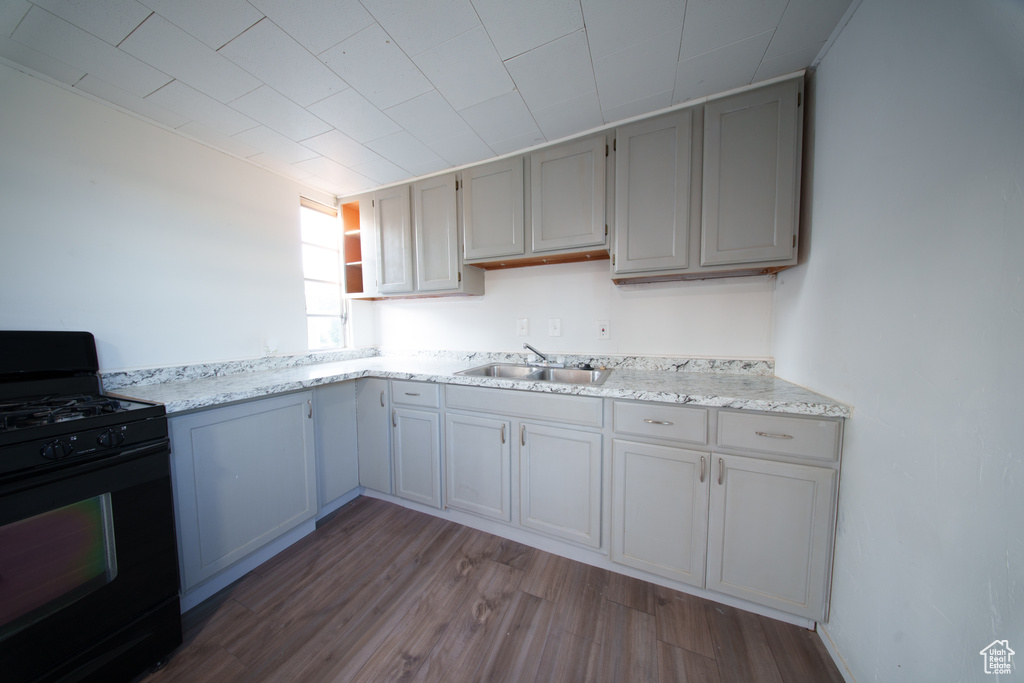 Kitchen featuring black range with gas cooktop, wood finished floors, open shelves, and light stone countertops