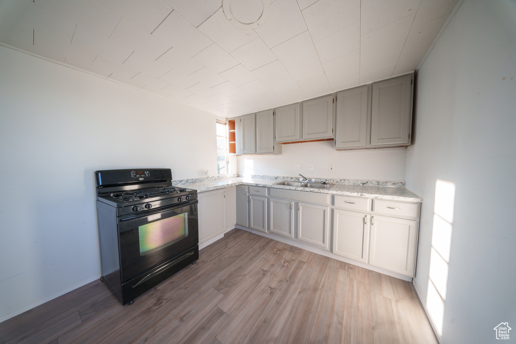 Kitchen featuring black gas range oven, light wood finished floors, gray cabinetry, and light stone counters