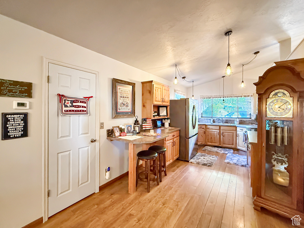 Kitchen featuring freestanding refrigerator, light wood-style flooring, light countertops, light brown cabinets, and lofted ceiling