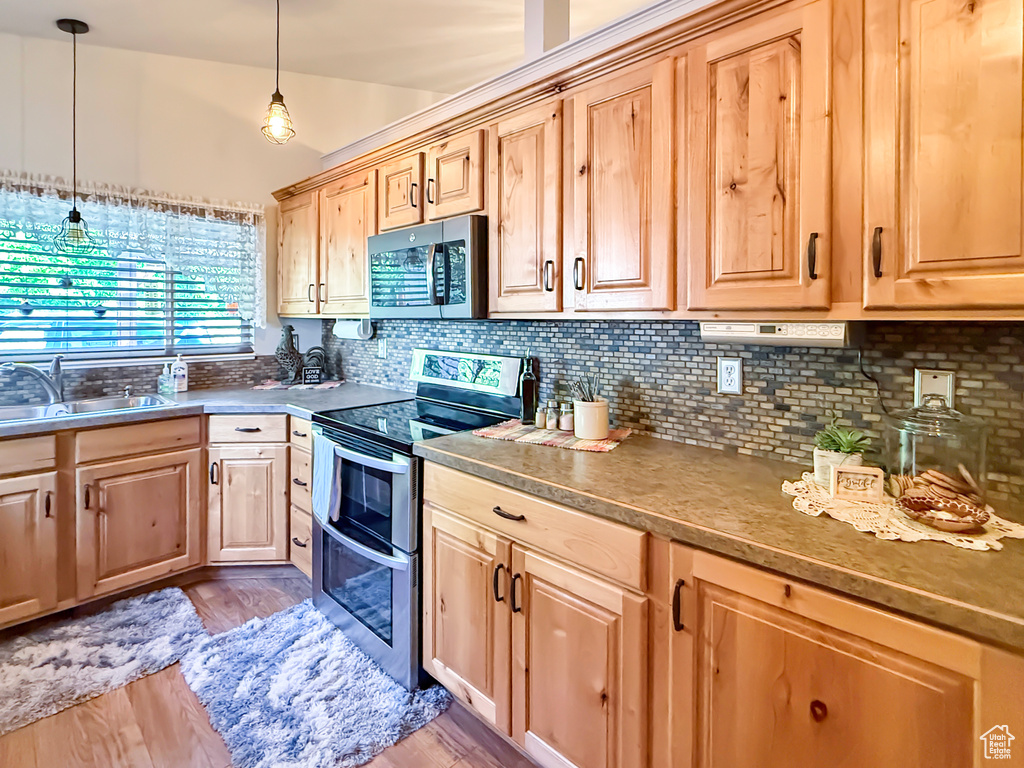 Kitchen featuring stainless steel appliances, light brown cabinets, backsplash, light wood-style floors, and hanging light fixtures