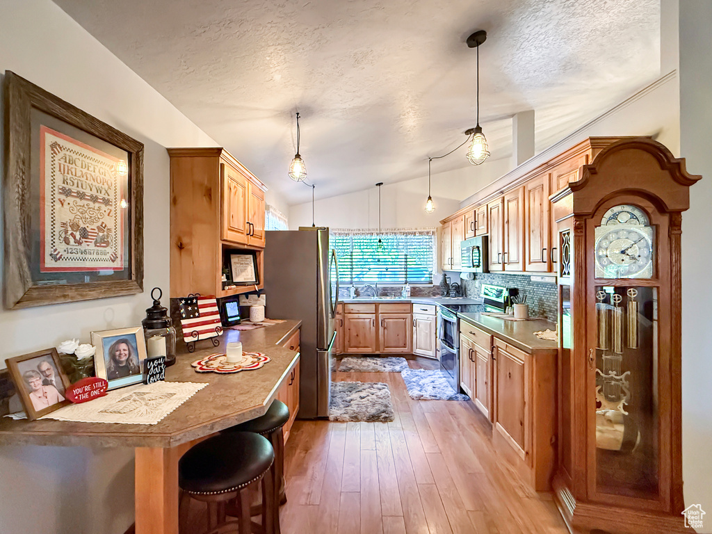 Kitchen with stainless steel appliances, a textured ceiling, lofted ceiling, light wood finished floors, and a breakfast bar area