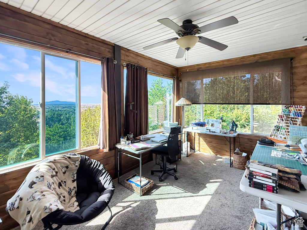 Carpeted home office with ceiling fan and wood walls