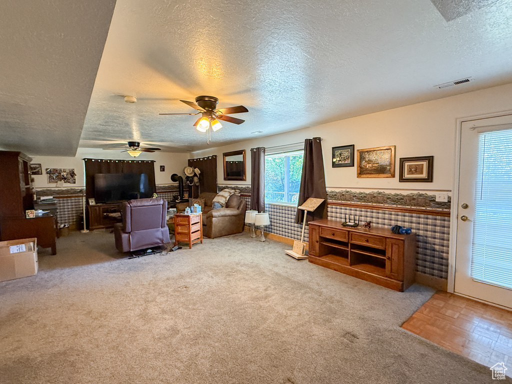 Living room with a textured ceiling, ceiling fan, wainscoting, and carpet floors