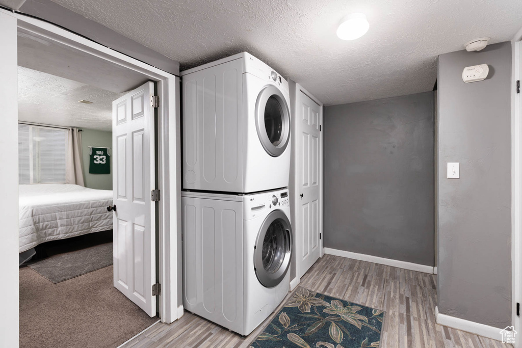 Laundry area featuring estacked washer and dryer, a textured ceiling, and light wood finished floors