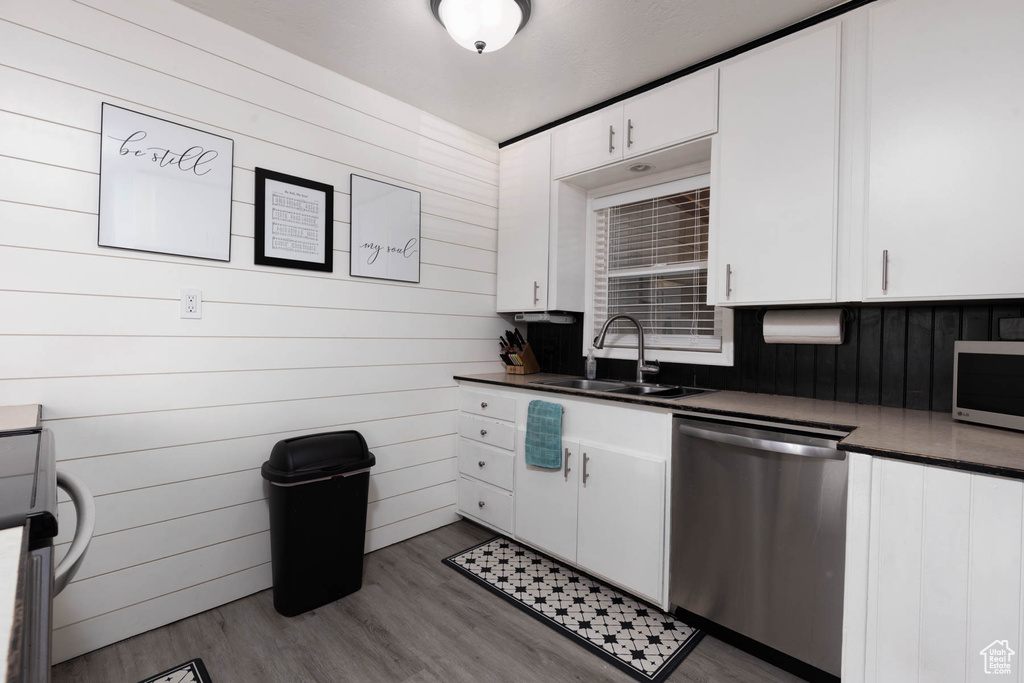 Kitchen featuring appliances with stainless steel finishes, dark countertops, white cabinetry, wood finished floors, and wooden walls