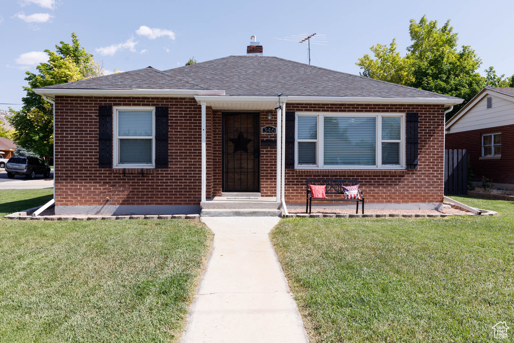 Bungalow-style home featuring brick siding, a front lawn, a chimney, and a shingled roof