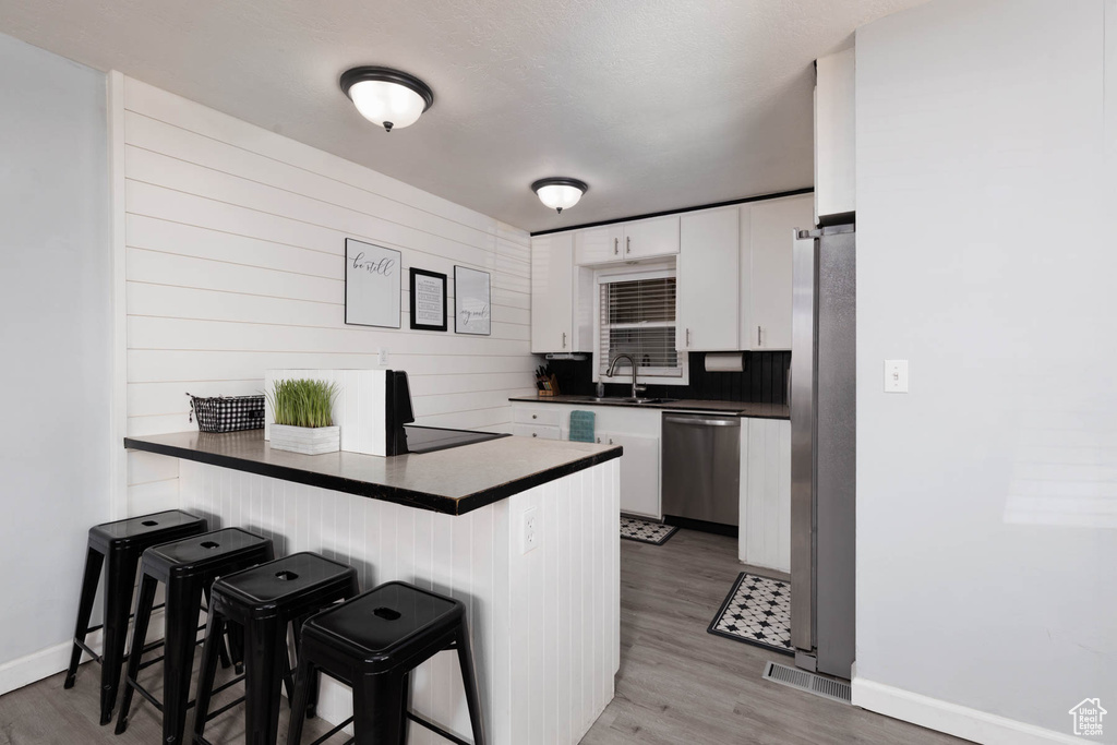 Kitchen featuring appliances with stainless steel finishes, dark countertops, a kitchen breakfast bar, a peninsula, and white cabinets