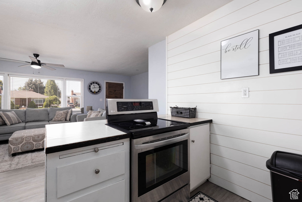 Kitchen with stainless steel electric range, light wood finished floors, white cabinetry, open floor plan, and ceiling fan