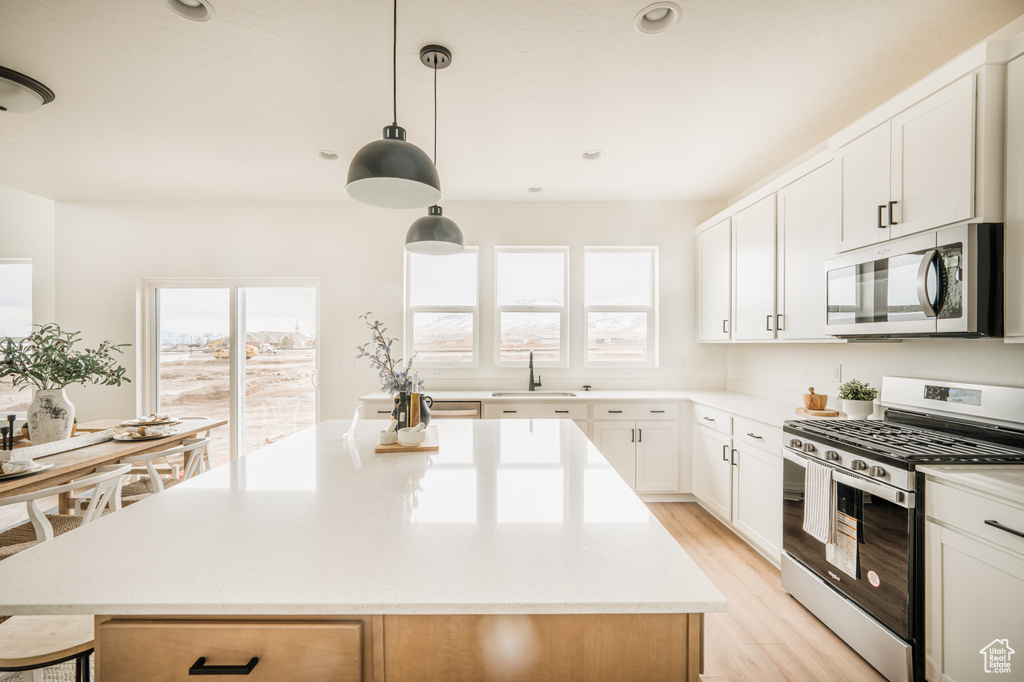 Kitchen featuring stainless steel appliances, light countertops, light wood-style floors, a center island, and white cabinetry