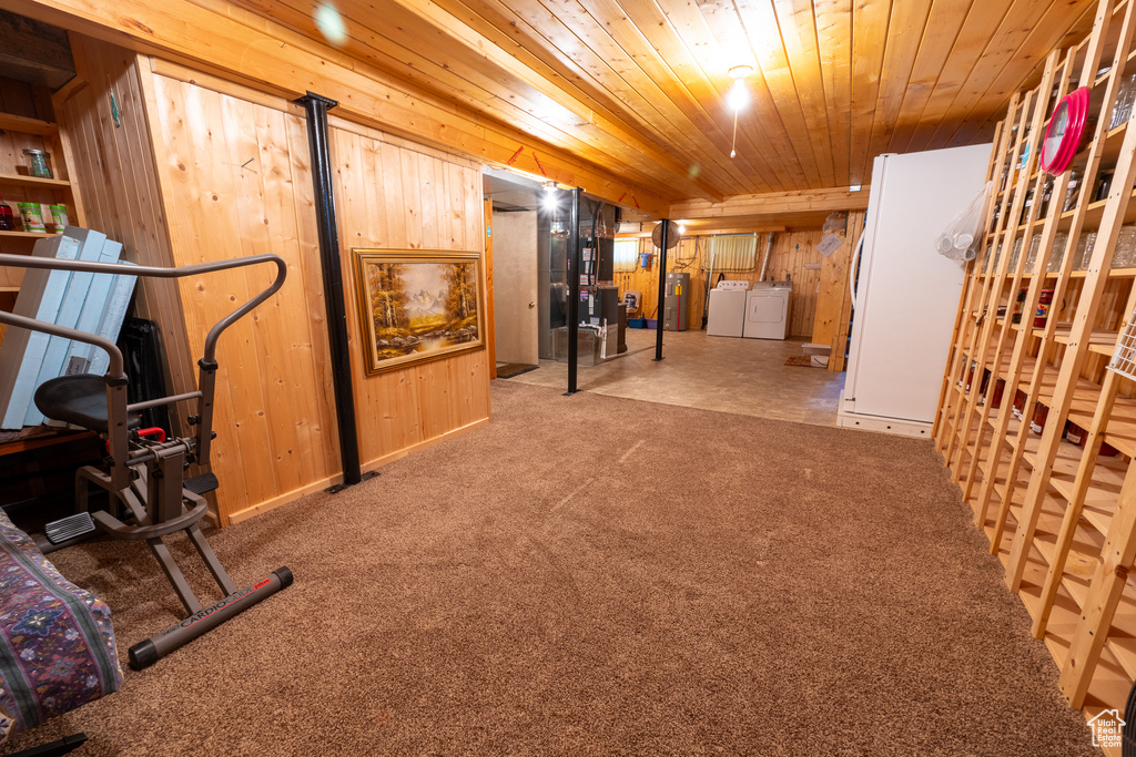 Finished below grade area featuring washing machine and clothes dryer, wood ceiling, wooden walls, carpet flooring, and freestanding refrigerator