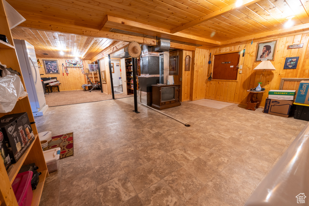 Finished basement with wood ceiling, wood walls, a wood stove, and tile patterned floors