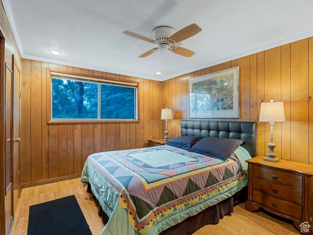 Bedroom featuring wood finished floors, ornamental molding, wood walls, and ceiling fan