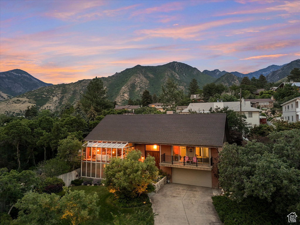 Back of property at dusk with concrete driveway, a mountain view, a sunroom, a chimney, and a garage