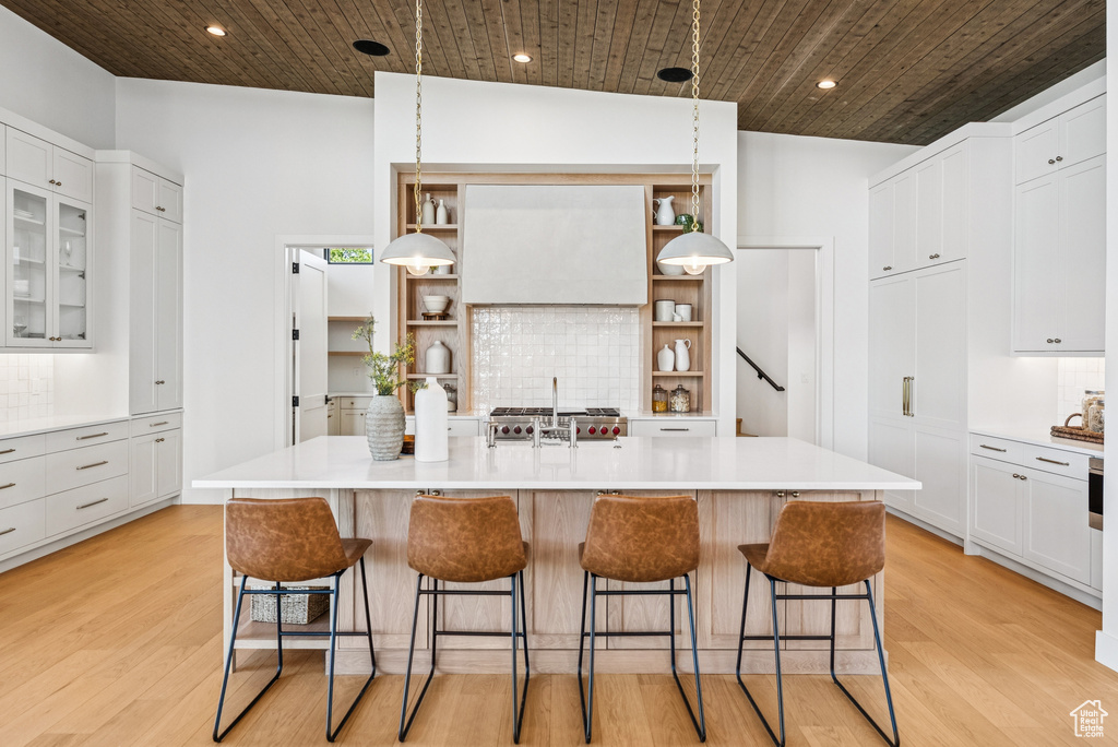 Kitchen with open shelves, a breakfast bar area, light wood-style floors, light countertops, and wood ceiling