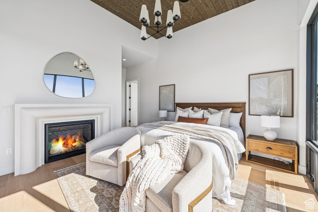 Bedroom featuring wooden ceiling, a chandelier, wood finished floors, high vaulted ceiling, and a glass covered fireplace