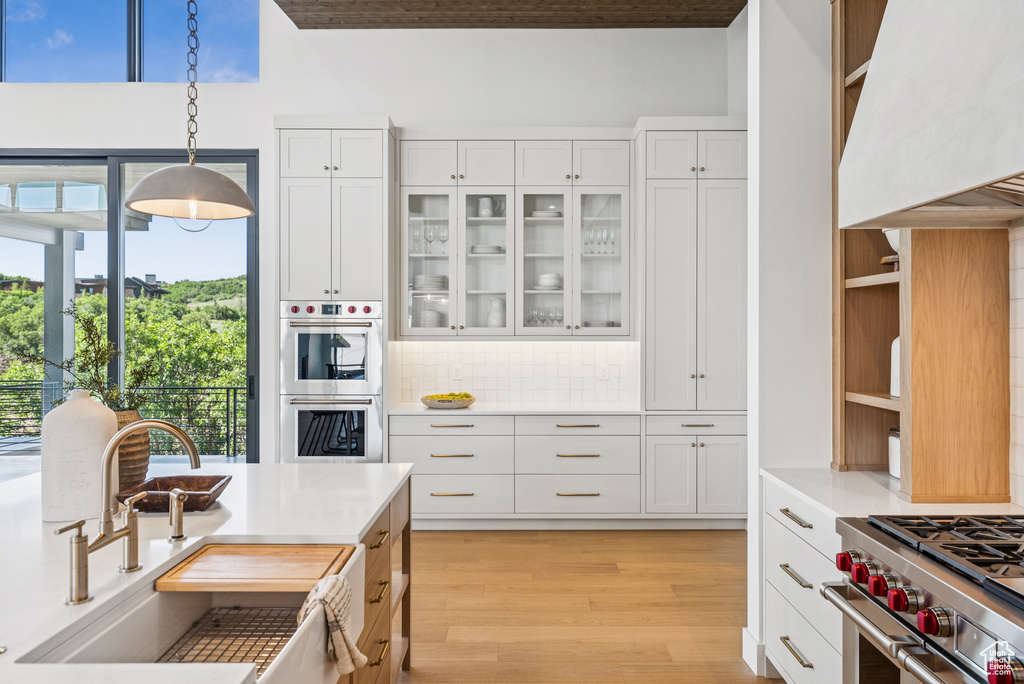 Kitchen with custom range hood, appliances with stainless steel finishes, decorative backsplash, light countertops, and white cabinets