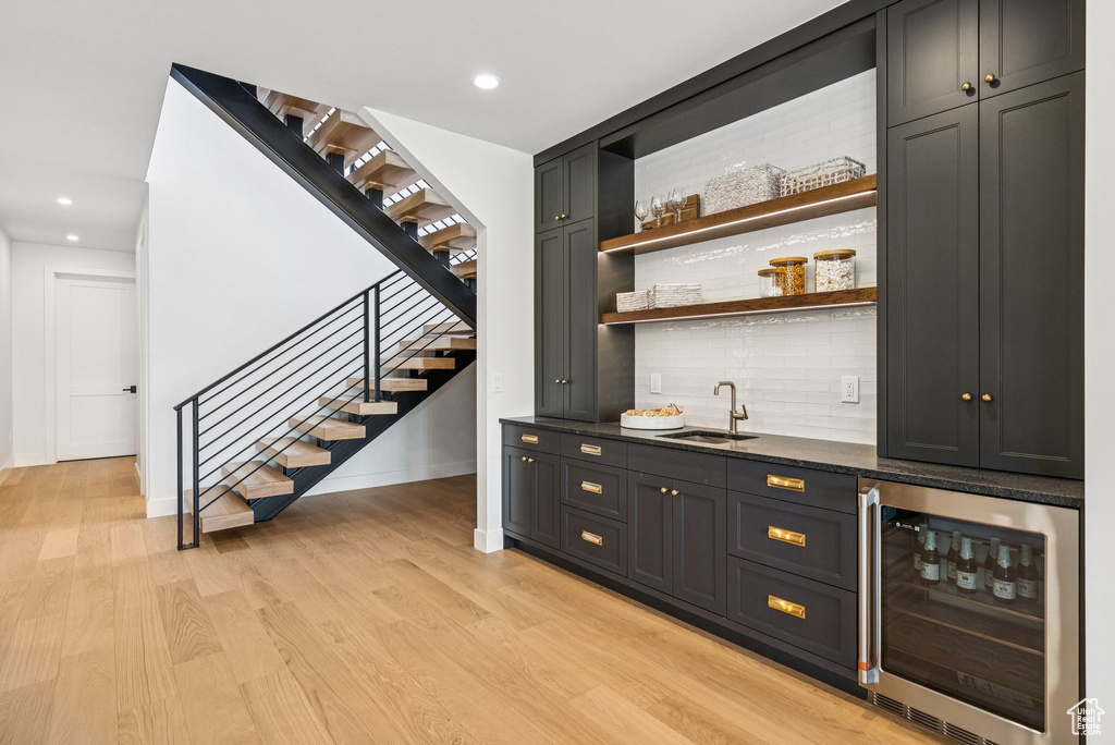 Indoor wet bar featuring beverage cooler, light wood-style floors, stairway, tasteful backsplash, and recessed lighting