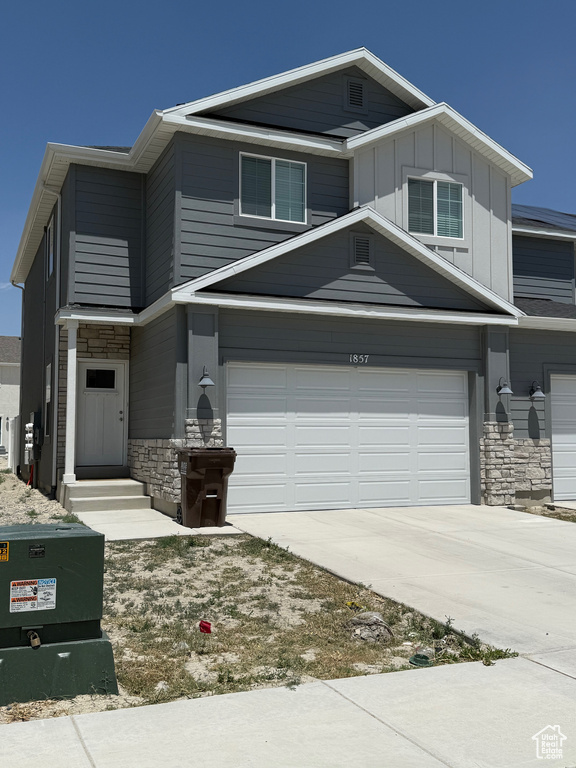 View of front of home with stone siding, driveway, and board and batten siding