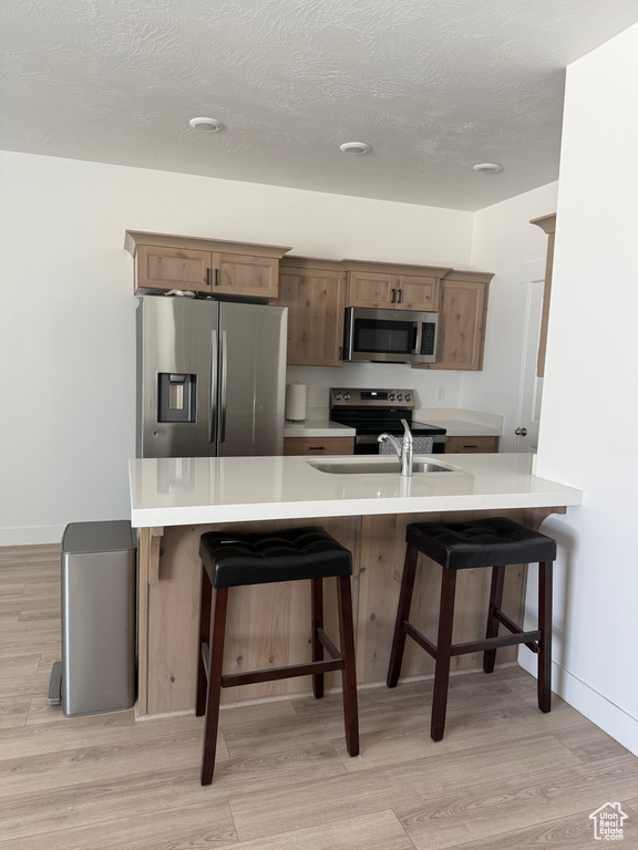 Kitchen with appliances with stainless steel finishes, light wood-type flooring, a kitchen breakfast bar, light countertops, and a textured ceiling