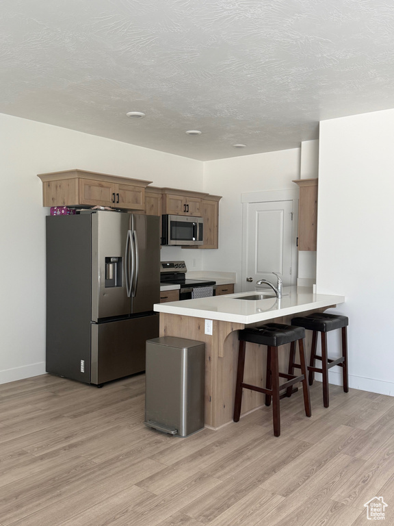 Kitchen featuring stainless steel appliances, a peninsula, light wood-style flooring, a kitchen bar, and light countertops
