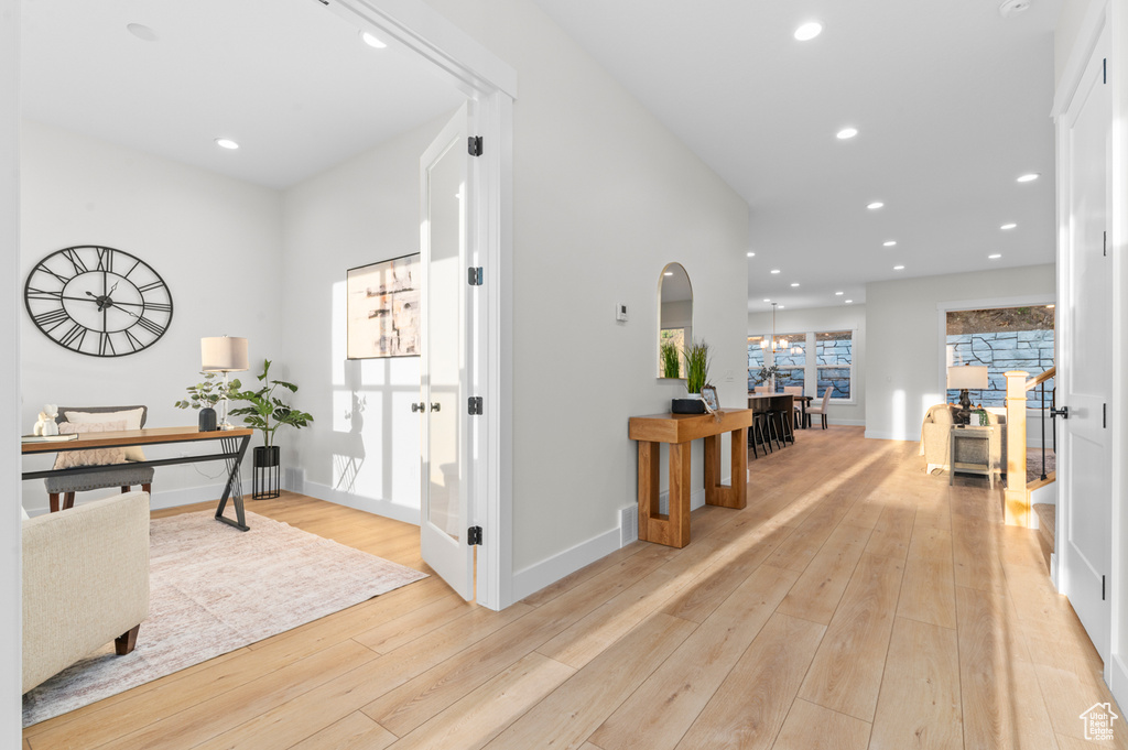 Corridor featuring light wood-style floors, arched walkways, recessed lighting, and a desk