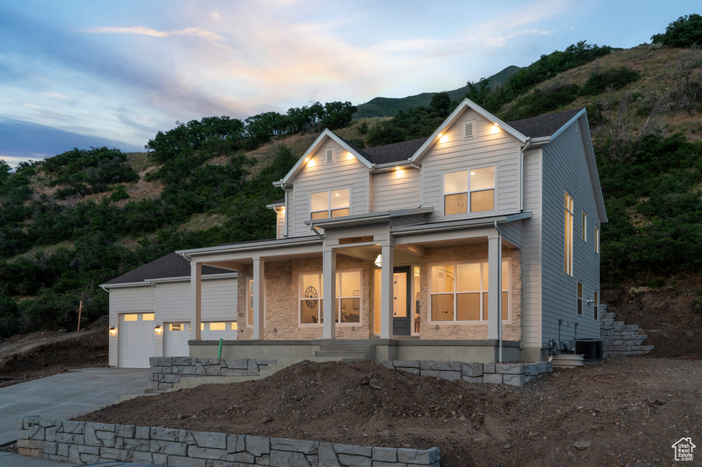View of front facade featuring a porch, concrete driveway, an attached garage, stone siding, and a mountain view