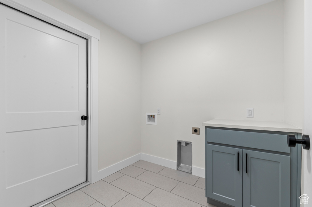Washroom with hookup for an electric dryer, washer hookup, cabinet space, and light tile patterned flooring