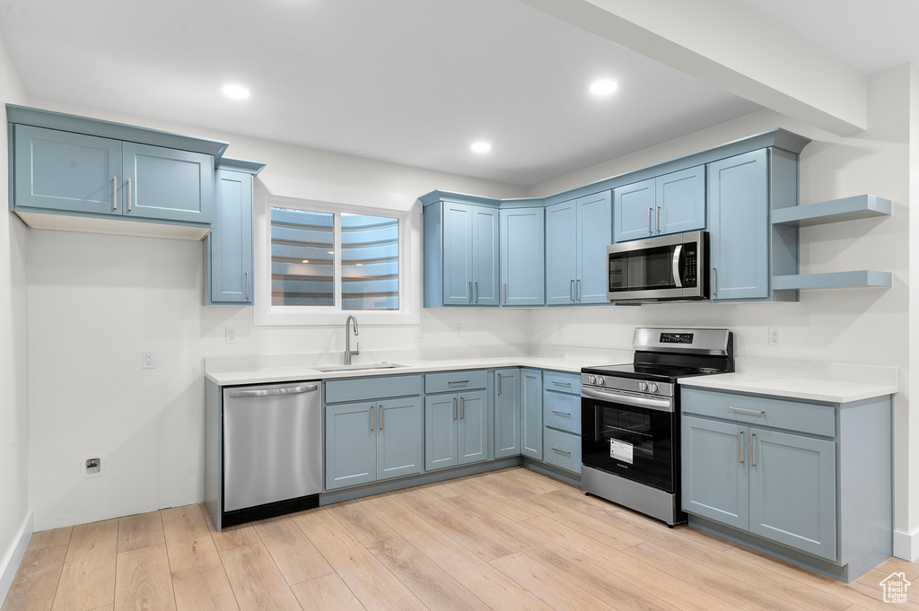 Kitchen with appliances with stainless steel finishes, blue cabinetry, open shelves, light countertops, and light wood-style flooring