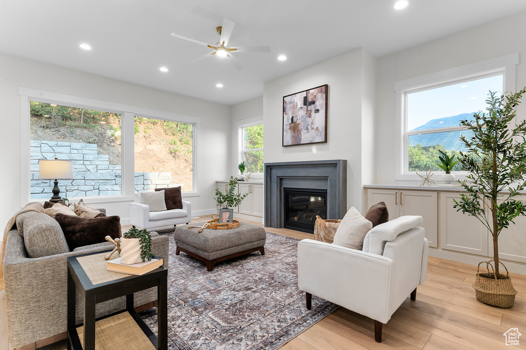 Living area with light wood-type flooring, ceiling fan, recessed lighting, and a glass covered fireplace