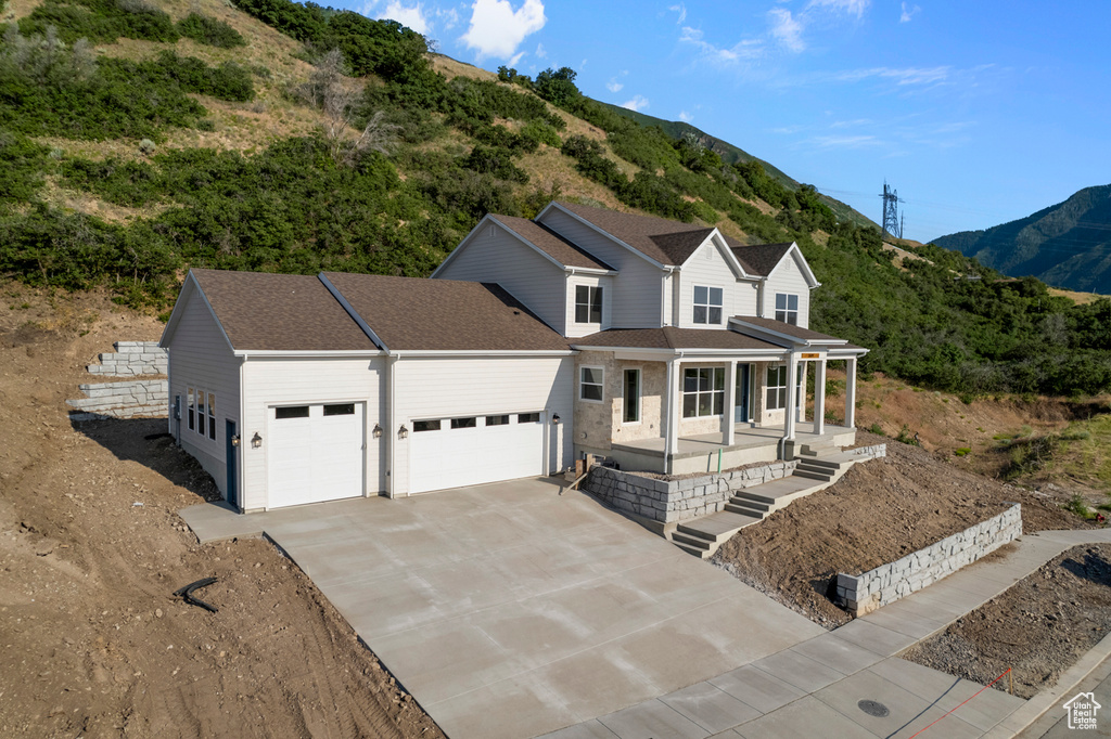 View of front of property featuring covered porch, an attached garage, a mountain view, concrete driveway, and roof with shingles