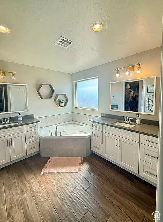 Bathroom with a bath, two vanities, wood finished floors, a textured ceiling, and recessed lighting