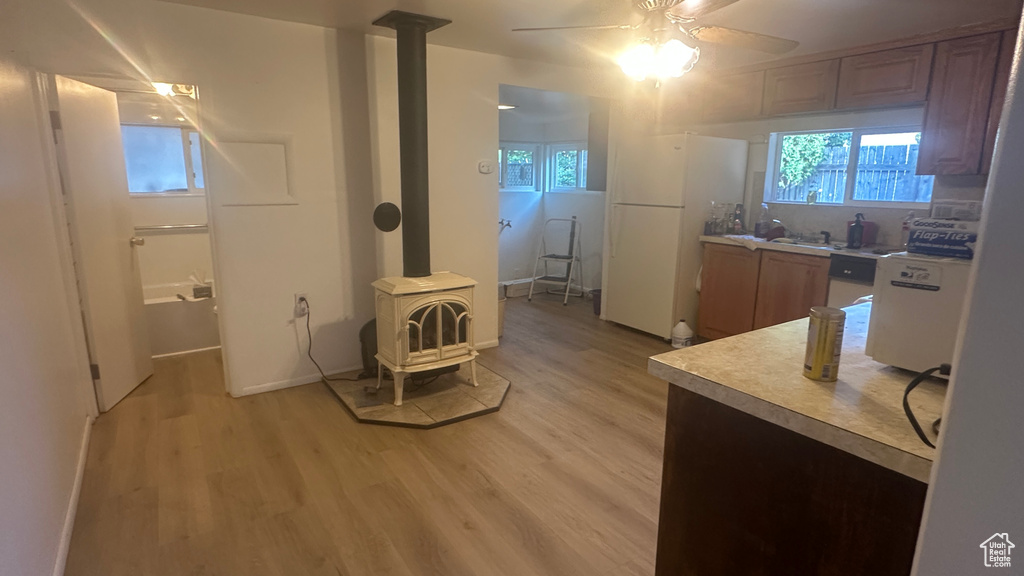 Kitchen featuring a wood stove, freestanding refrigerator, ceiling fan, light countertops, and light wood finished floors
