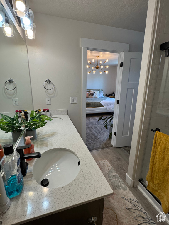 Ensuite bathroom featuring double vanity, a shower stall, wood finished floors, a chandelier, and a textured ceiling
