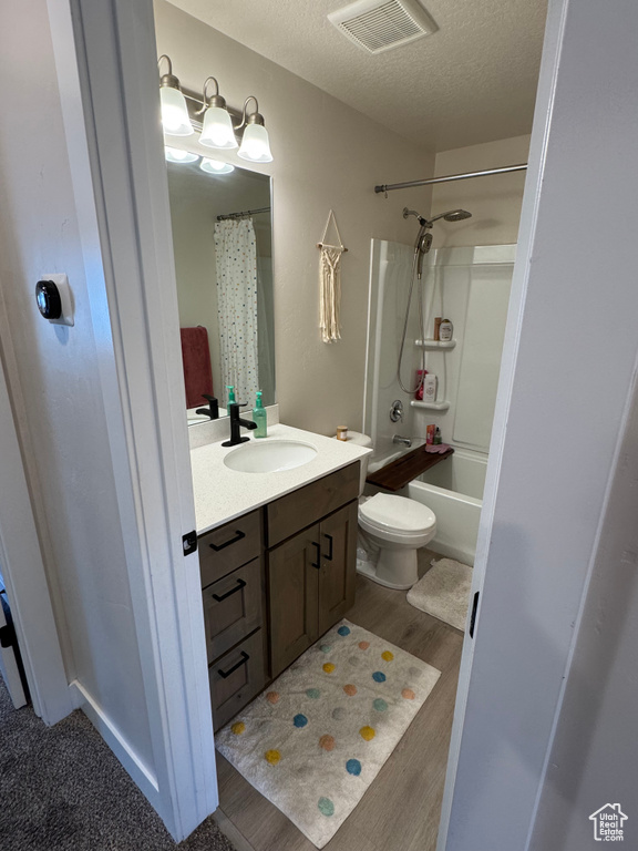 Full bath with vanity, a textured ceiling, shower / bathtub combination with curtain, and wood finished floors