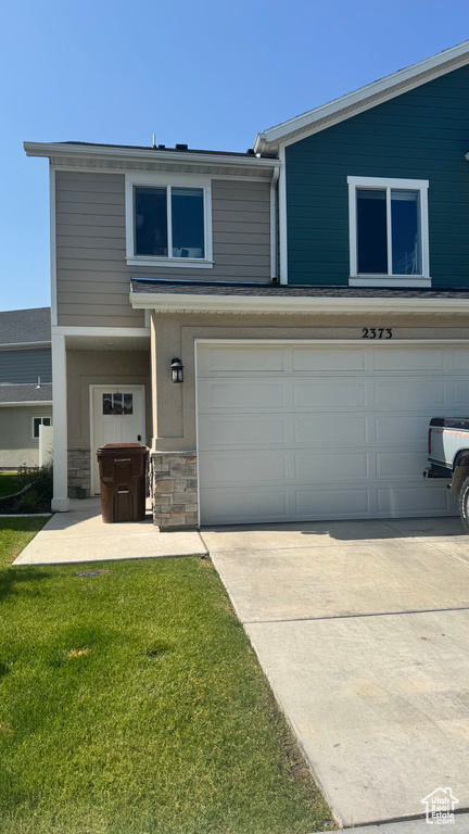 Traditional home with an attached garage, stone siding, driveway, and a front lawn