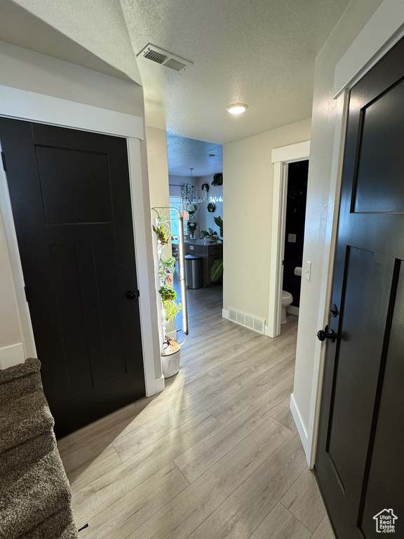 Foyer entrance with a textured ceiling, light wood finished floors, and stairway