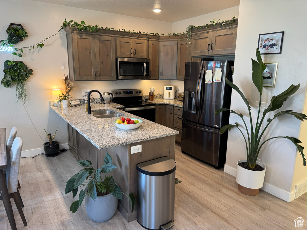 Kitchen featuring appliances with stainless steel finishes, a peninsula, light wood-style flooring, and light stone counters