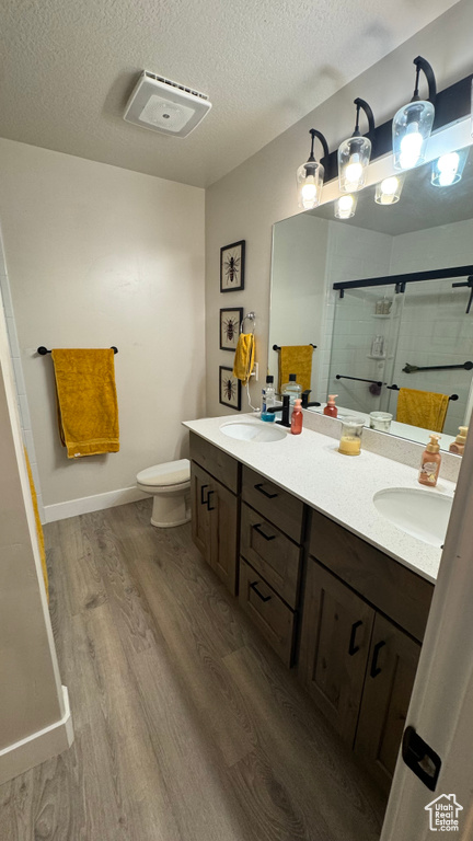 Full bathroom with wood finished floors, double vanity, a stall shower, and a textured ceiling