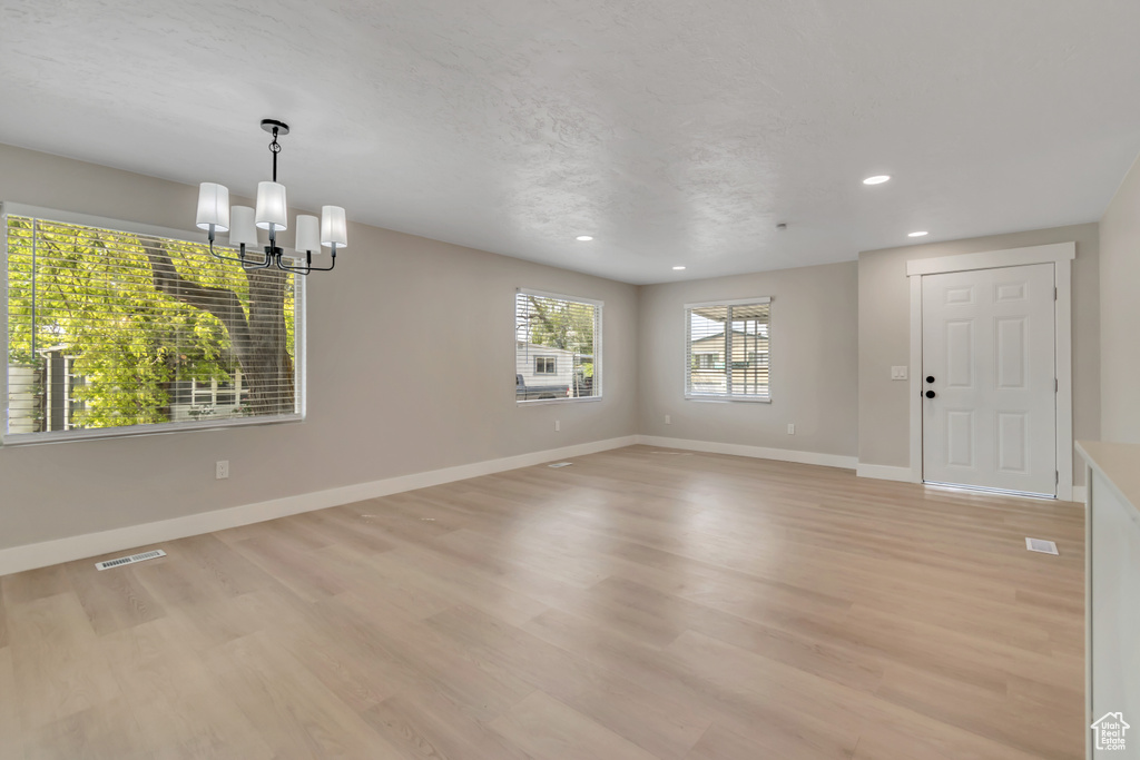 Empty room with a chandelier, light wood finished floors, and recessed lighting
