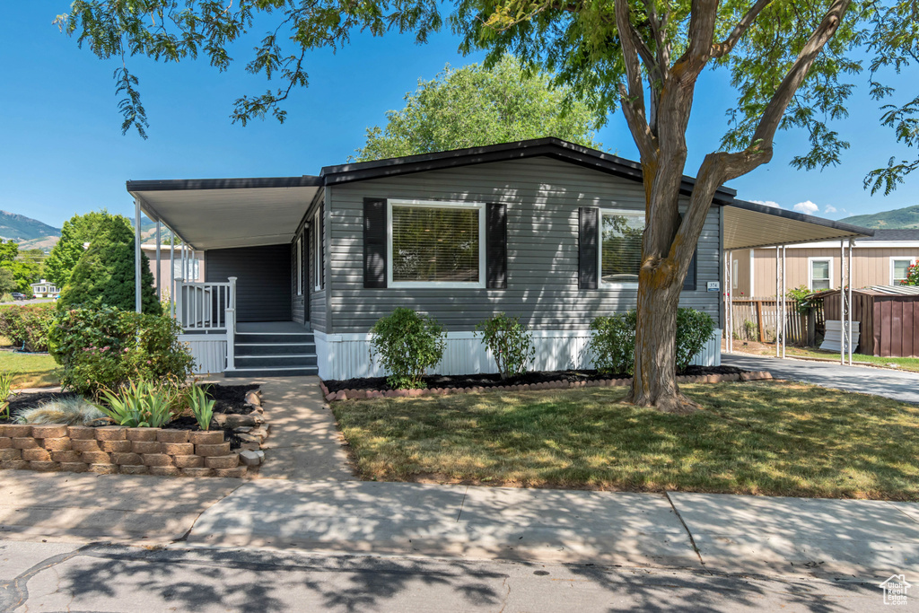 Manufactured / mobile home with a carport, a mountain view, a front lawn, concrete driveway, and covered porch