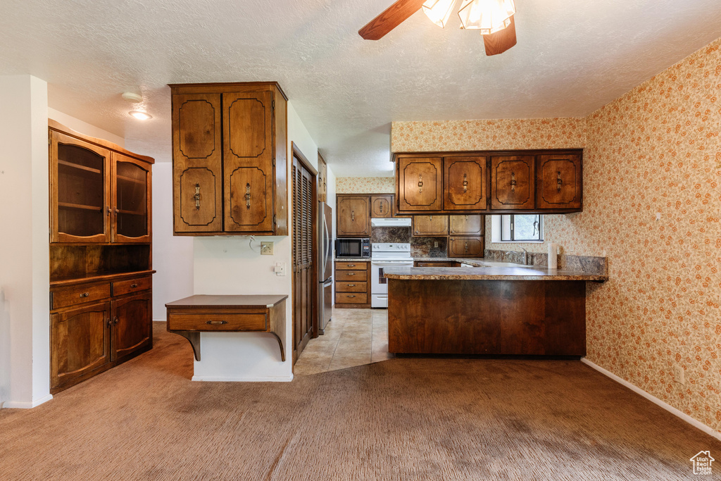 Kitchen featuring stainless steel appliances, wallpapered walls, a peninsula, light carpet, and ceiling fan