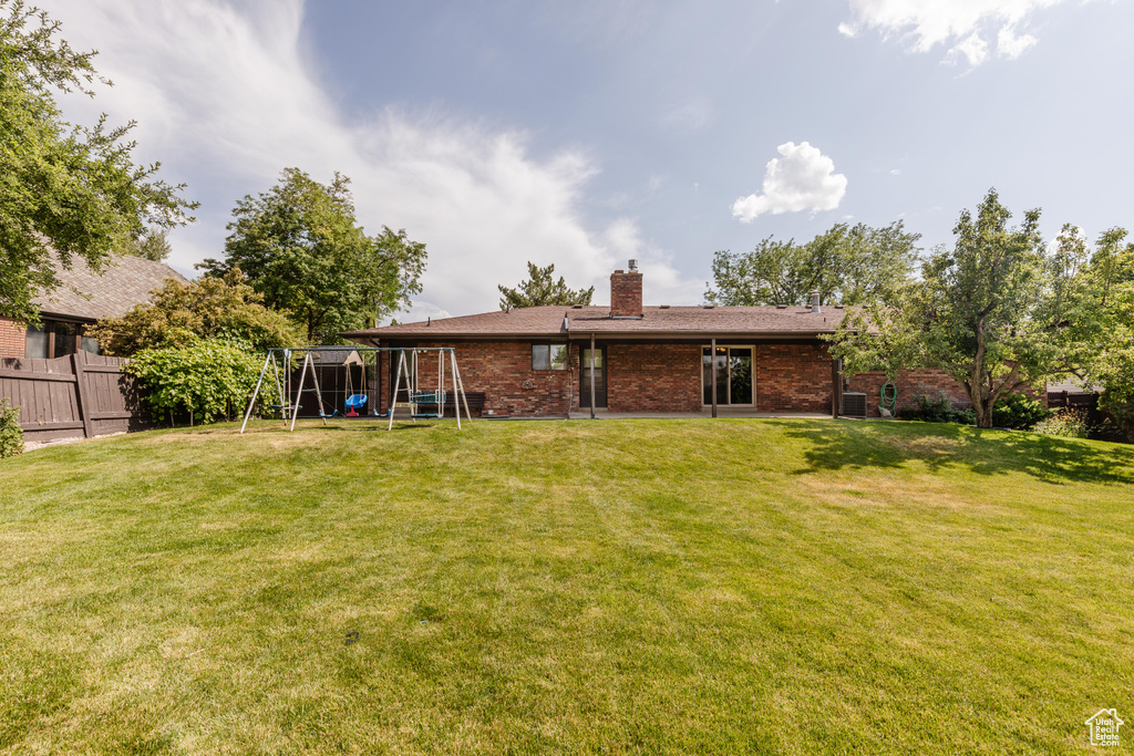 Back of property featuring a playground, a chimney, and brick siding