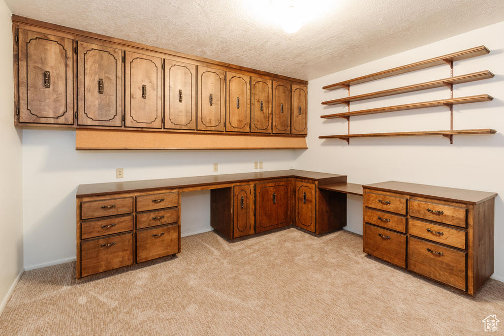 Unfurnished office featuring a textured ceiling, built in study area, and light carpet
