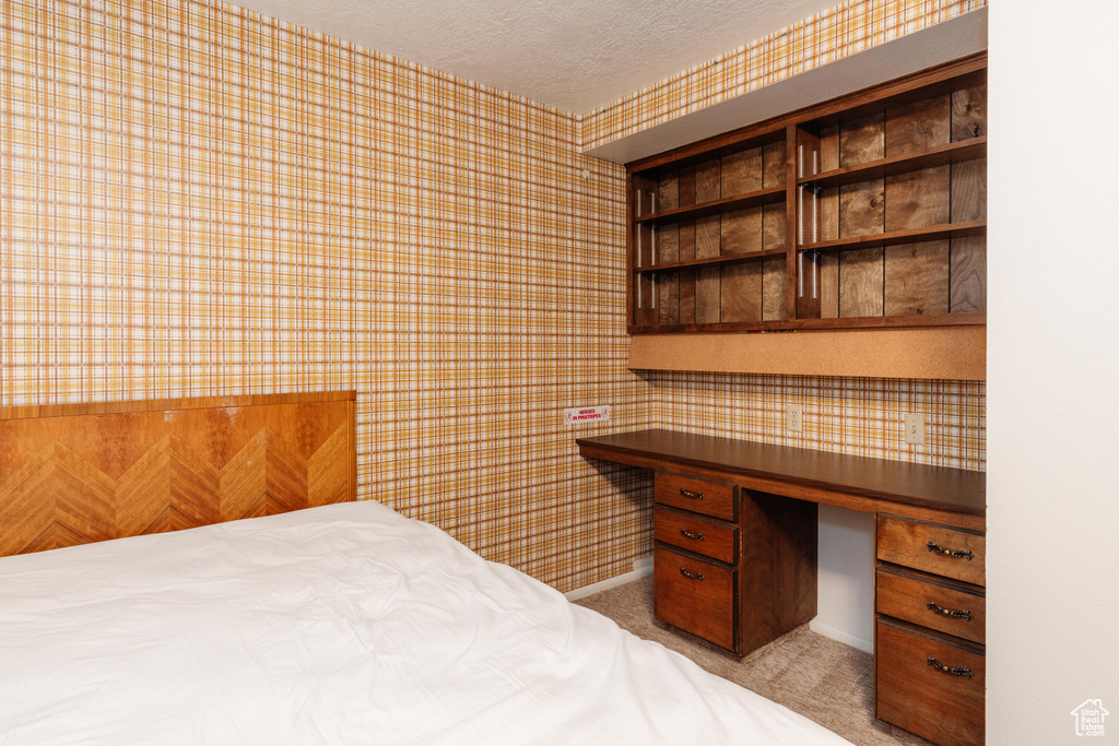 Bedroom featuring wallpapered walls, a textured ceiling, light carpet, and built in desk