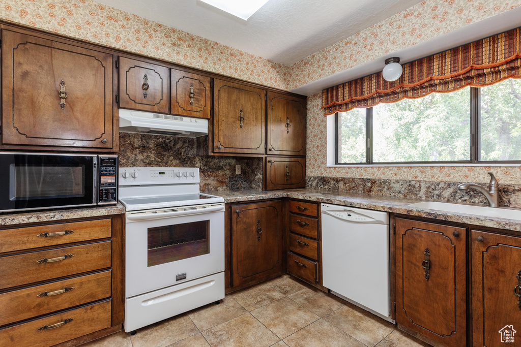 Kitchen with white appliances, under cabinet range hood, light tile patterned floors, backsplash, and light countertops