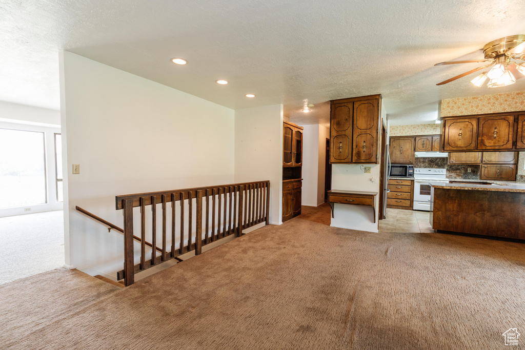 Kitchen with electric stove, light colored carpet, under cabinet range hood, recessed lighting, and ceiling fan