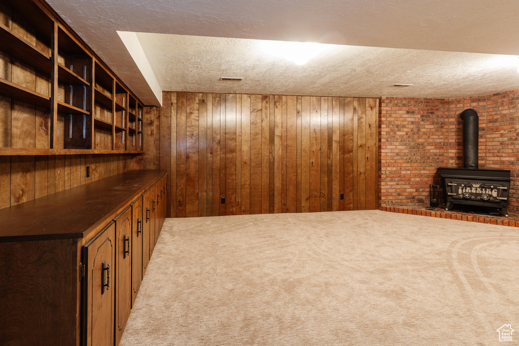 Finished basement featuring a textured ceiling, wood walls, a wood stove, and light carpet