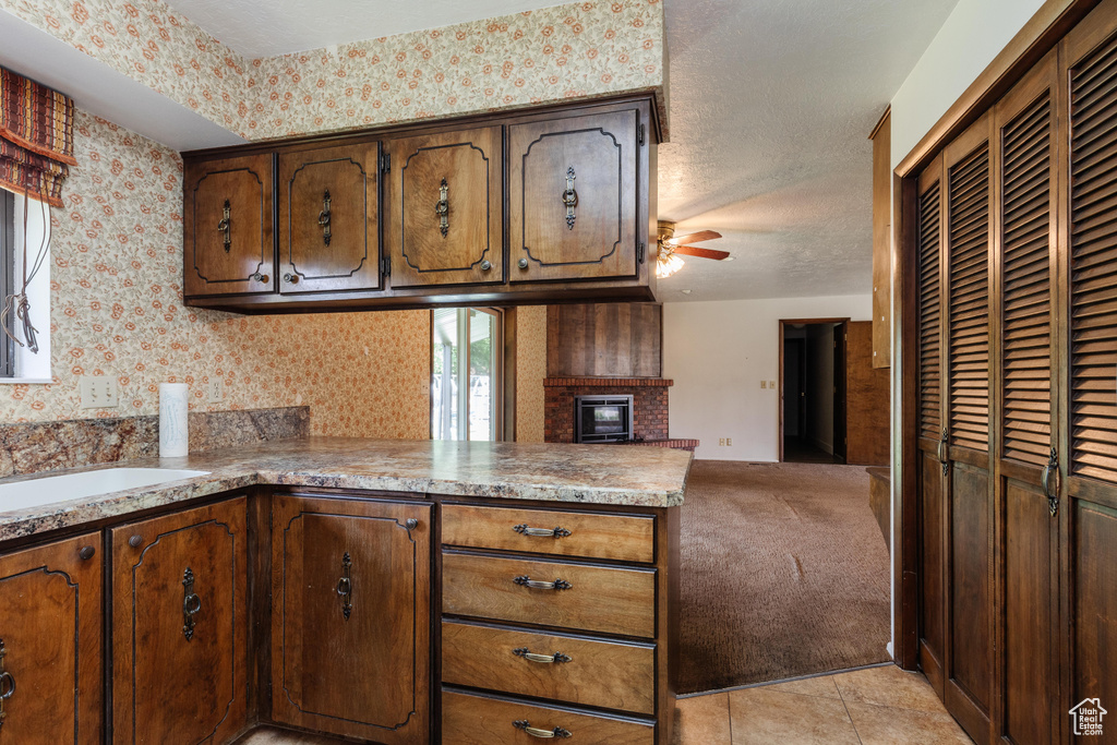 Kitchen with a peninsula, ceiling fan, wallpapered walls, open floor plan, and a fireplace