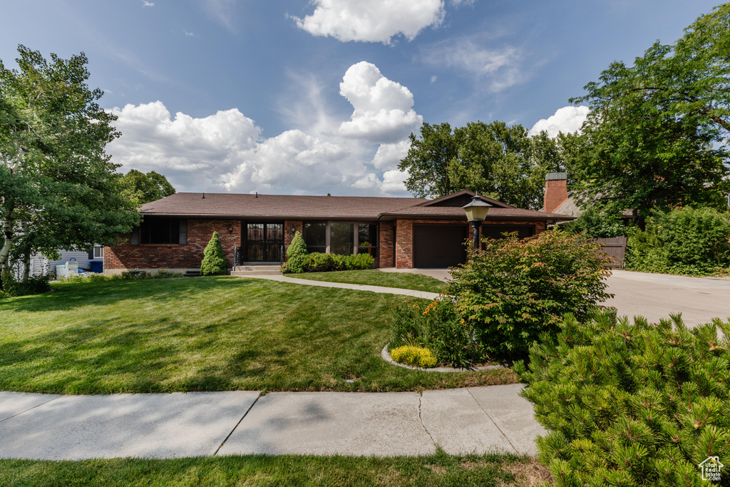 Single story home featuring an attached garage, brick siding, a front yard, and concrete driveway
